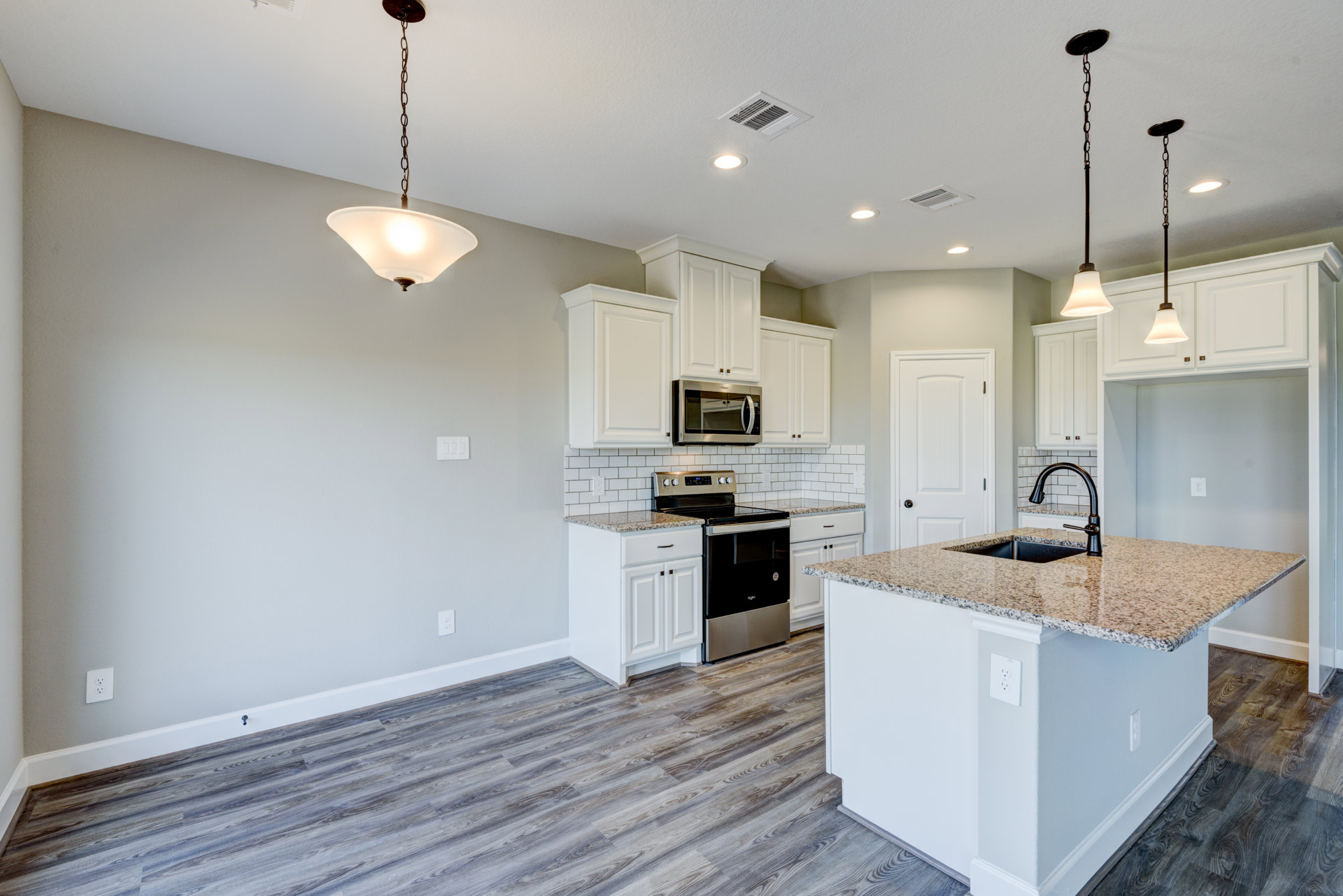 White kitchen cabinets, black appliances including open microwave, kitchen island with sink, stove and oven, tile backsplash, pendant light, metal support pole, light countertops