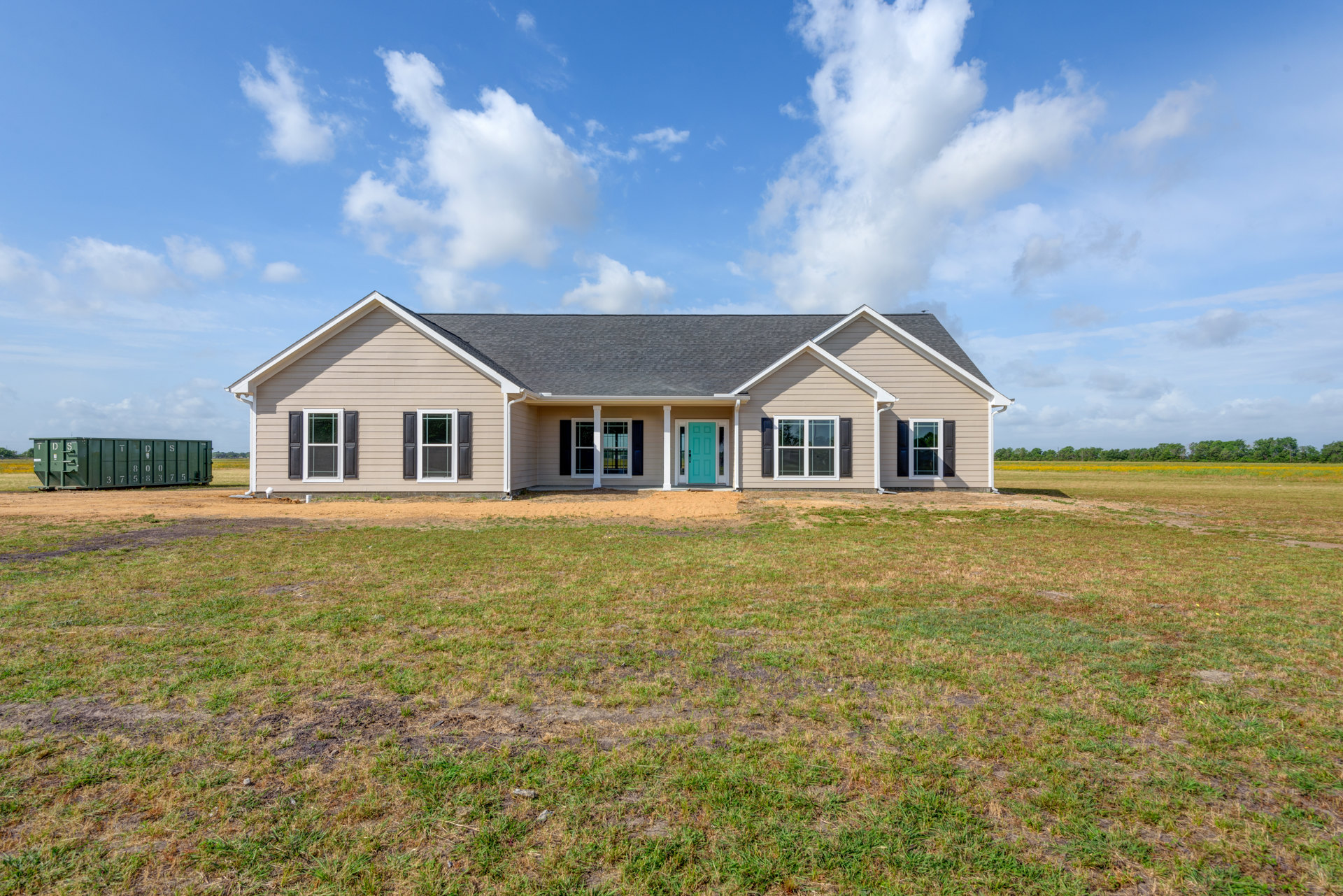 Blue front door with white trim and pillars, green grass lawn, white farmhouse-style exterior, windows, and cloudy blue sky.