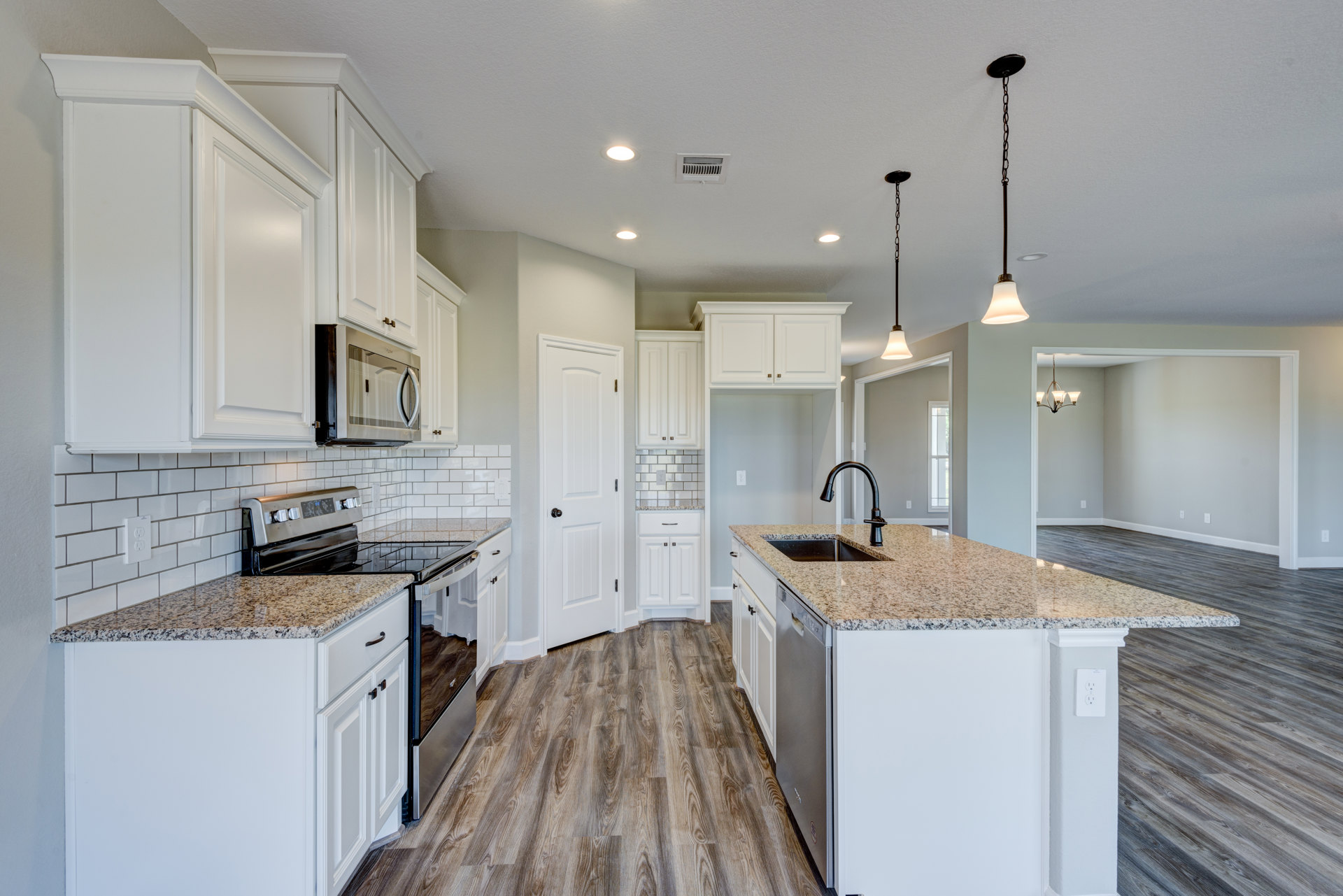 Kitchen with white shaker cabinets, granite countertops, wood flooring, stainless steel microwave, and a central island with matching granite surface