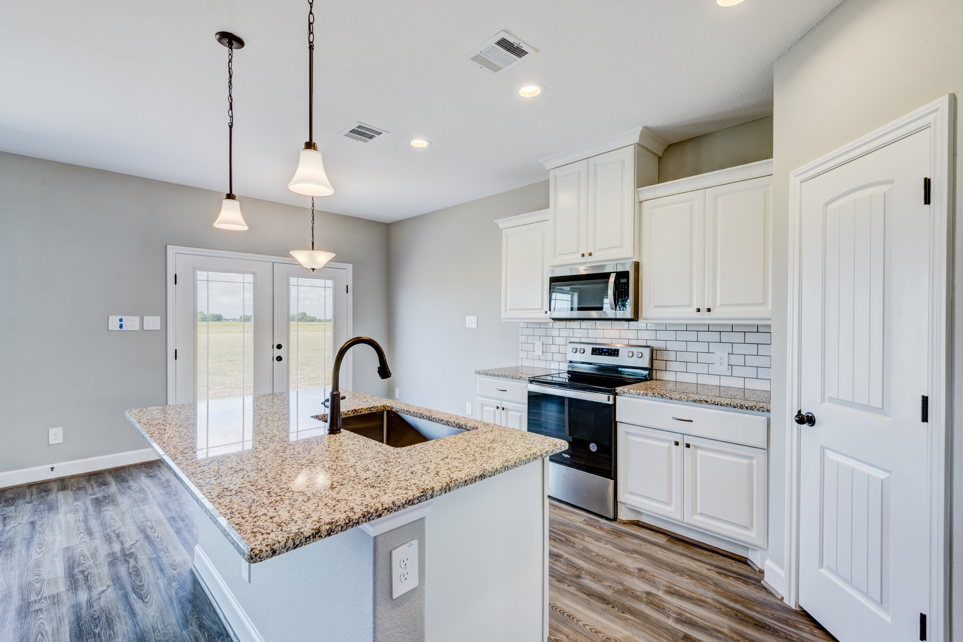 Marble kitchen countertop with black undermount sink, white outlet, built-in microwave, countertop oven, tile backsplash, and white cabinetry