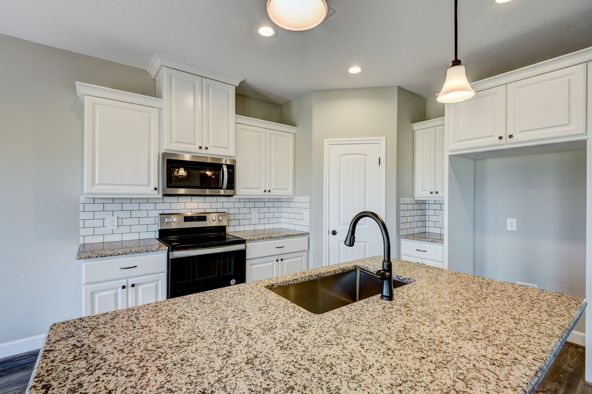 Kitchen with white shaker cabinets, granite countertops, stainless steel microwave with lights on, stove, undermount sink set in black granite, pendant light fixture hanging from