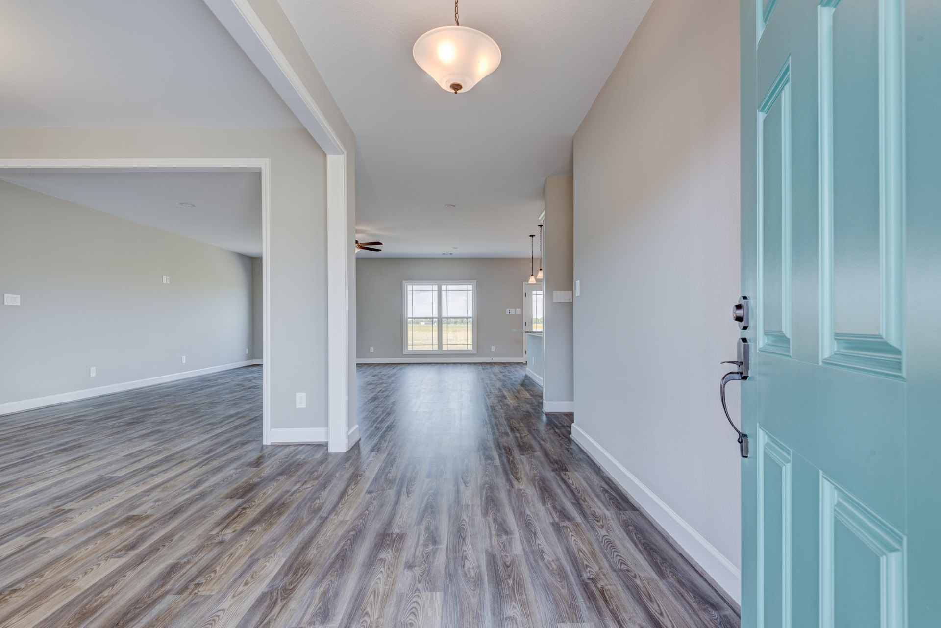 Hallway with blue door, wood flooring, white plaster walls, ceiling light fixture, window overlooking grassy field