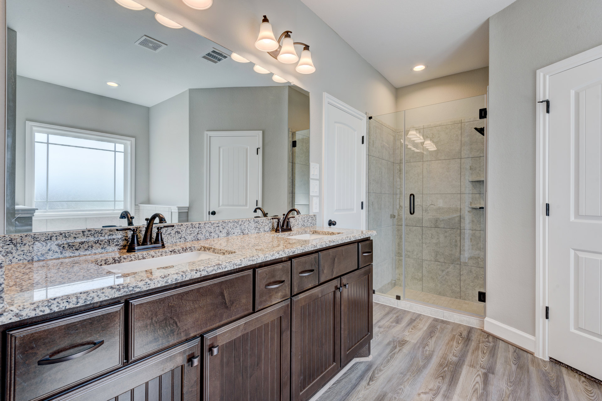 Bathroom featuring a glass shower enclosure, marble countertops, white cabinetry with black handles, frosted glass window, three-light fixture, and white door with black hinge