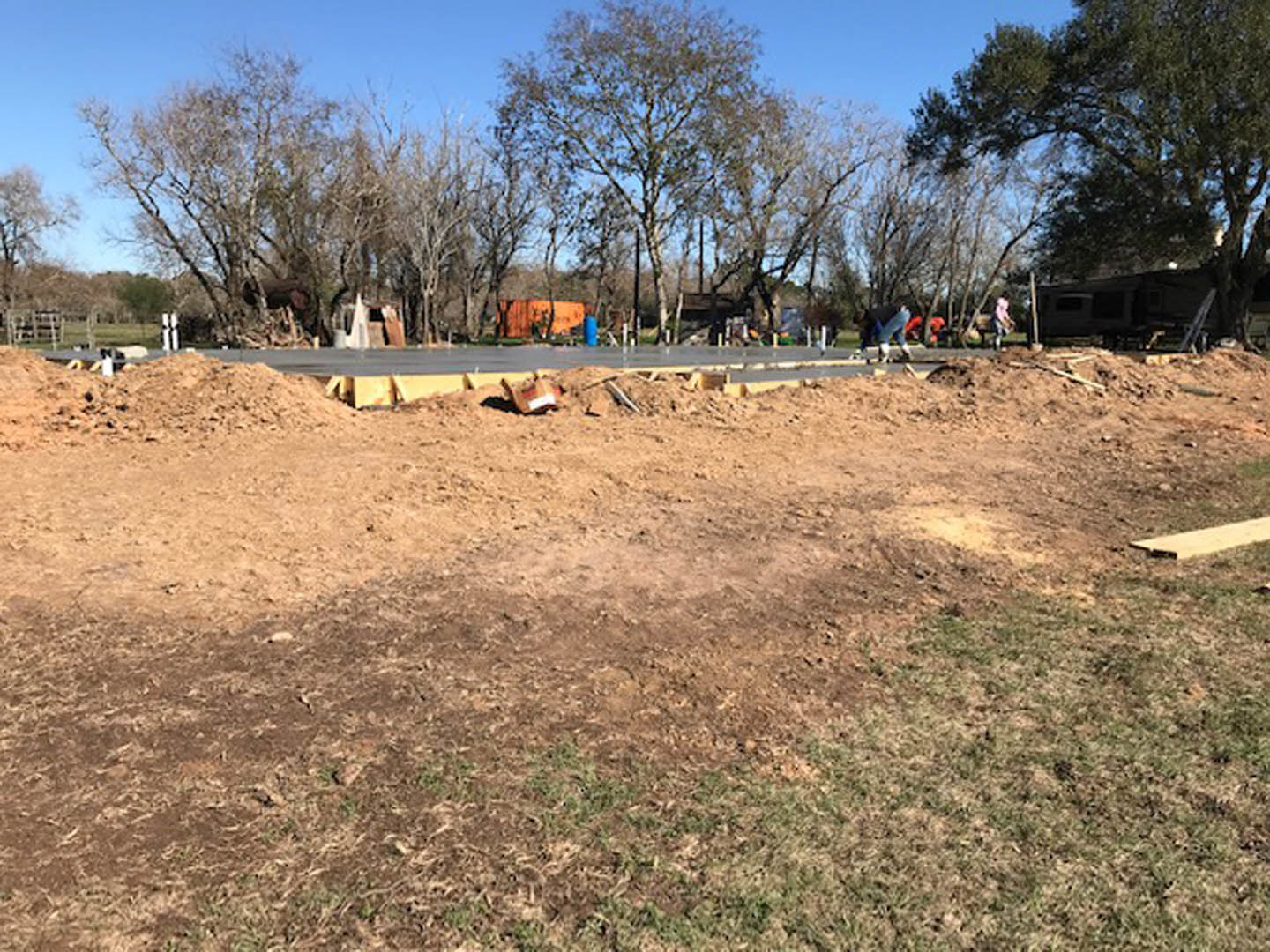 Dirt pile surrounded by trees and grass beside a paved road under a clear sky