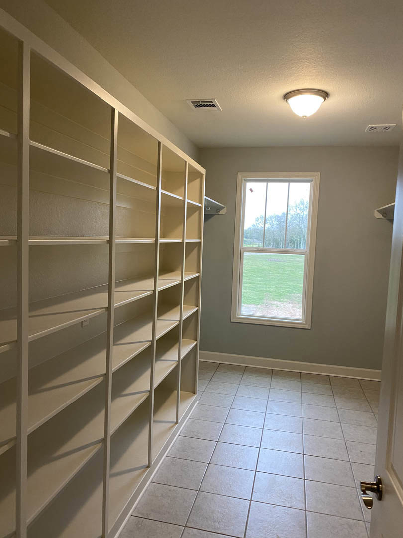 White tile floor, built-in white shelving along wall, large window overlooking grassy field, simple ceiling light fixture, close-up of brushed metal door knob
