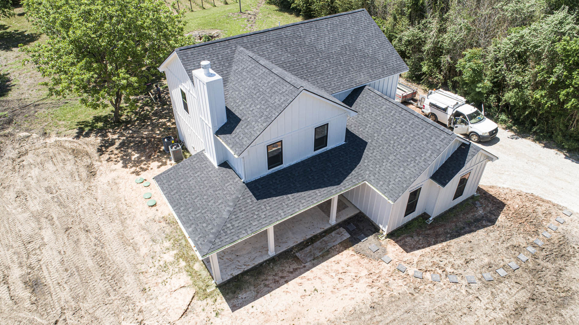 White siding house with black shingle roof, large window with white frame, parked white truck with open door, green-leafed tree in front yard