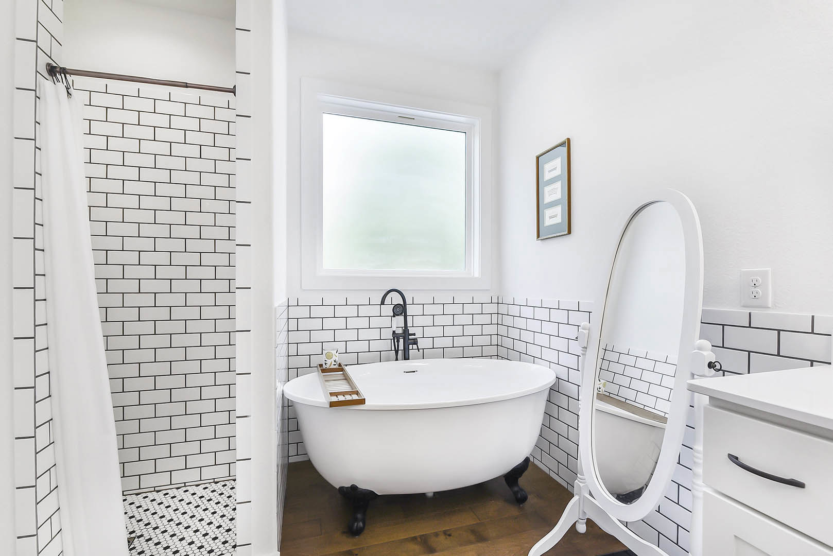 White bathroom featuring a freestanding tub, large wall mirror above a floating vanity with integrated sink, white tile walls, chrome faucet, and modern drawer cabinetry.