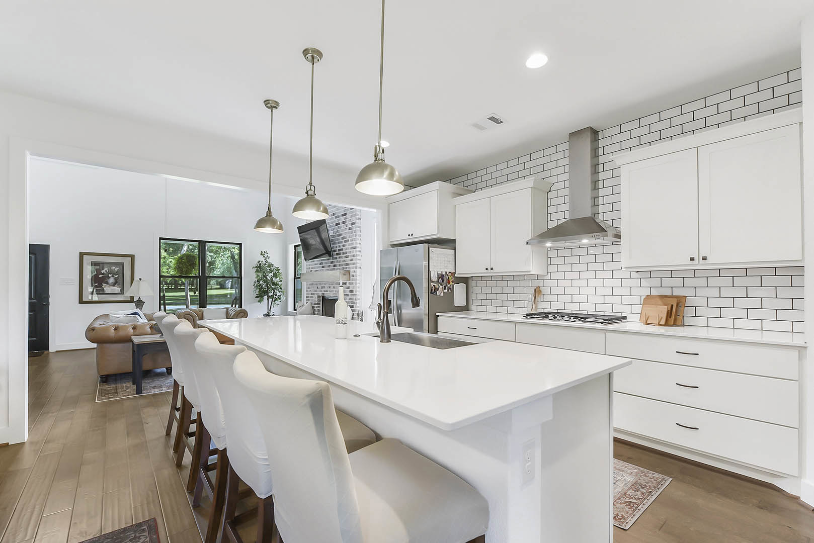 White kitchen featuring a spacious island with white countertop, large dining table, white cabinets with black handles, window overlooking trees, pole light fixture, and a person