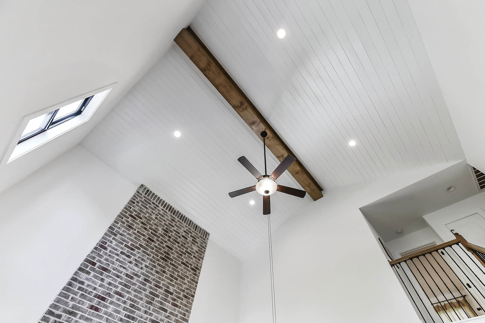 Ceiling fan with light fixture mounted near exposed brick chimney, white plaster walls, and wood beam accents