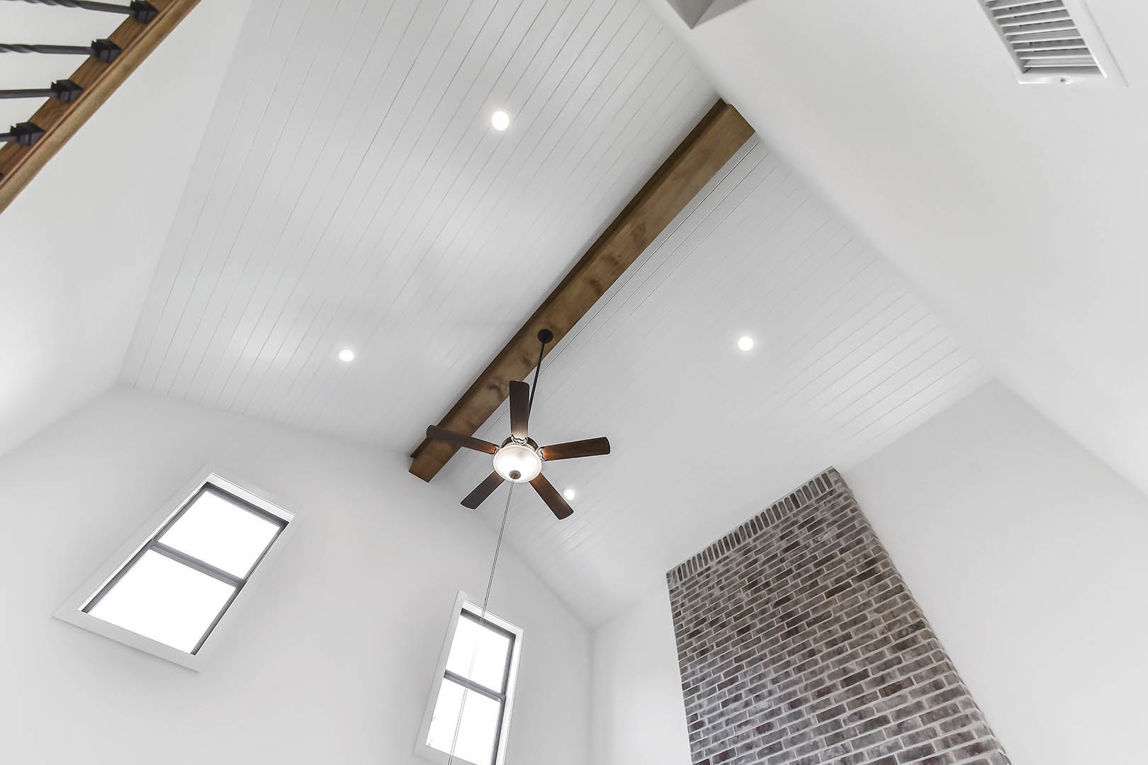 Ceiling fan with light fixture mounted on white plaster ceiling, exposed brick chimney, rectangular window with white trim, wooden ceiling beam