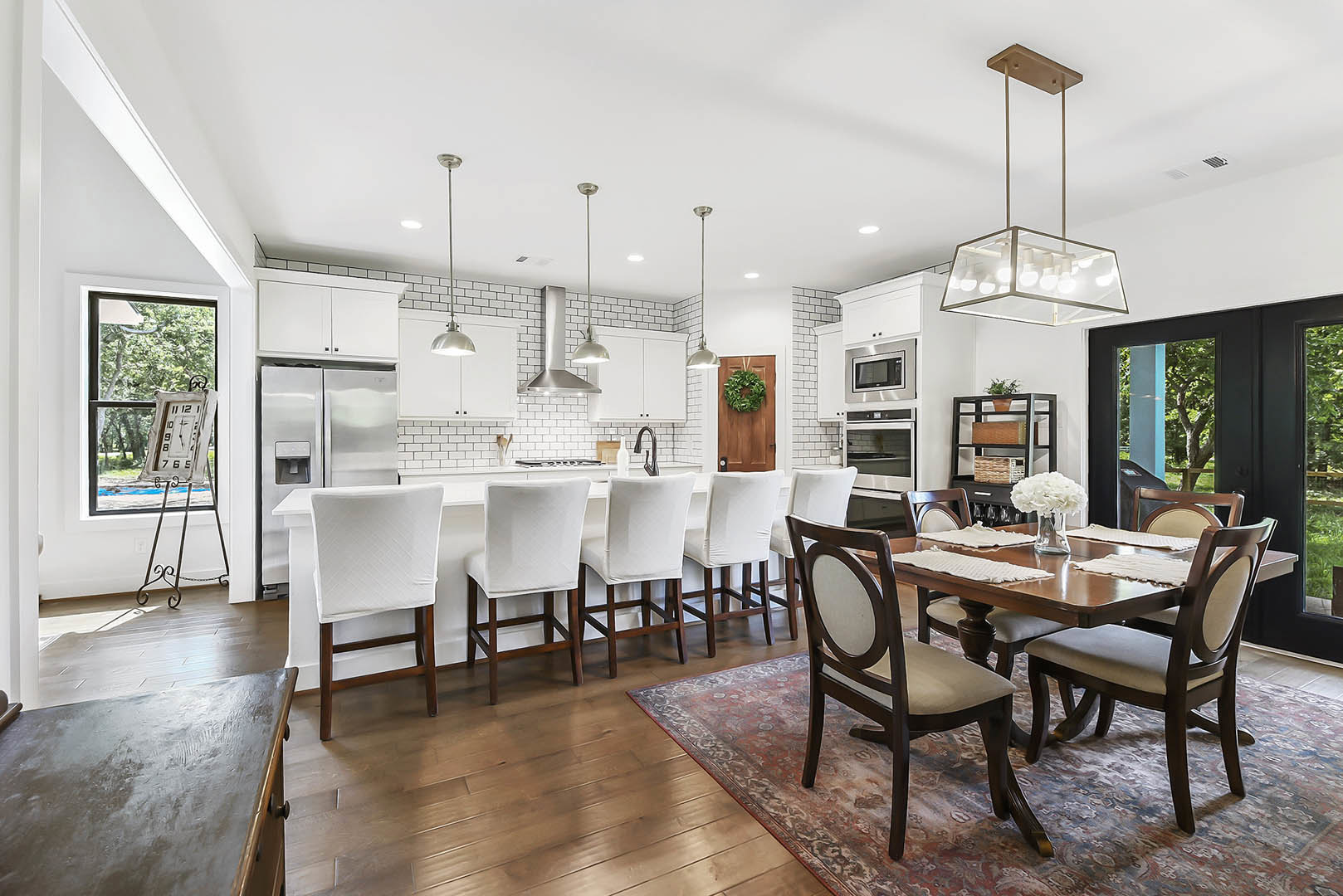 Open-concept kitchen and dining area featuring a wood dining table with white slipcovered chairs, light laminate flooring, white countertops, pendant light fixture, and a