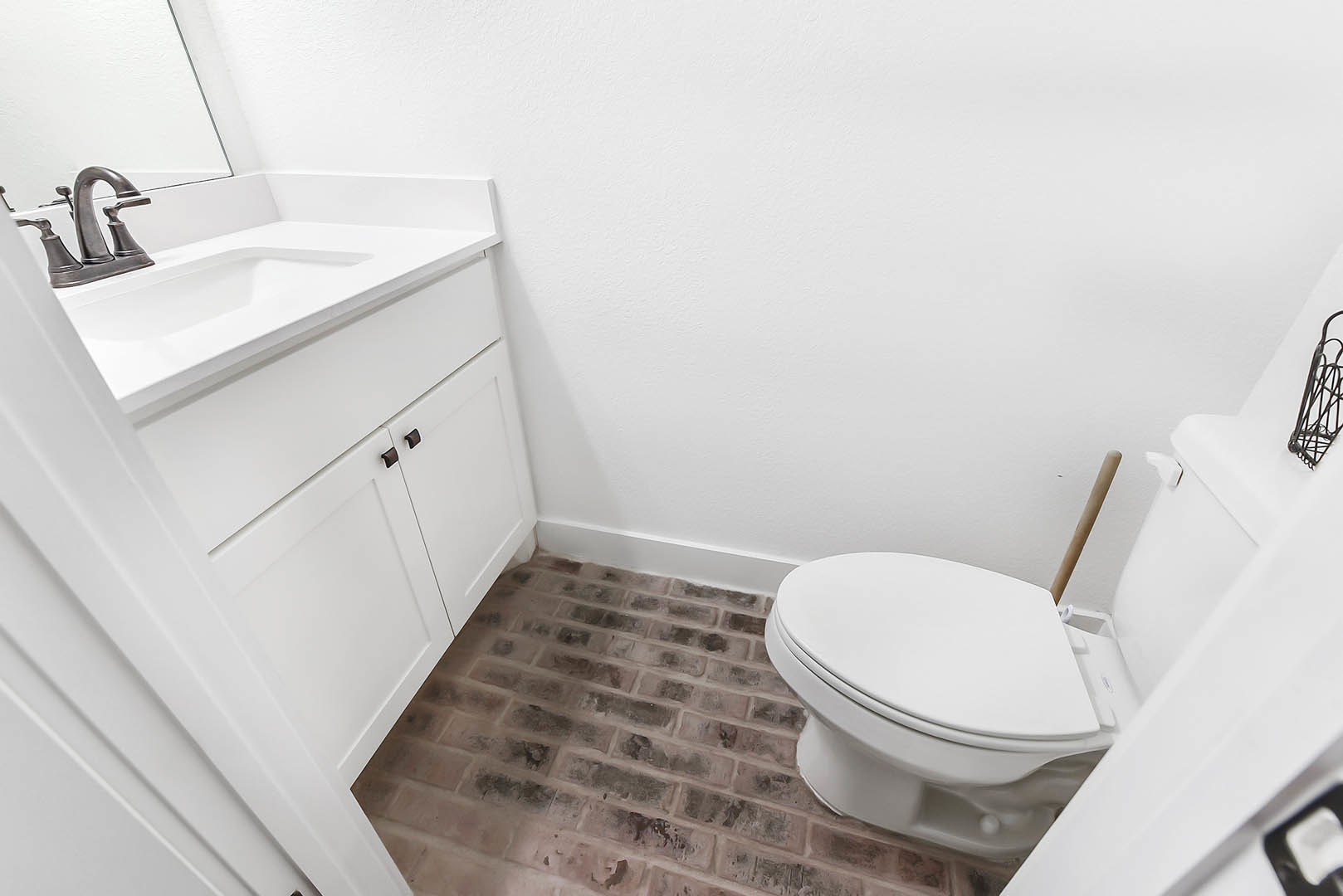 White porcelain toilet and rectangular sink with chrome faucet set against light tile walls in a modern bathroom; plunger positioned behind toilet.