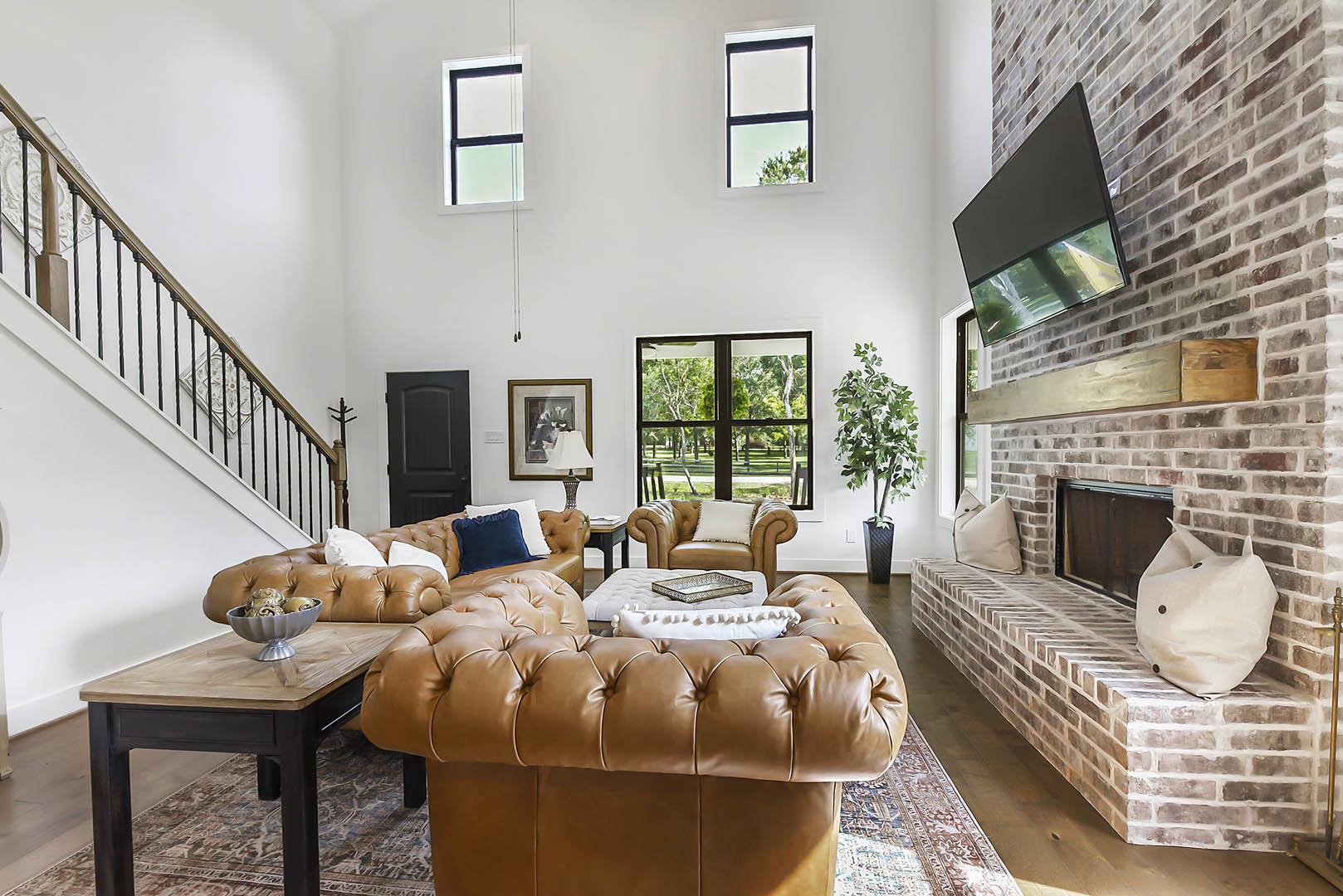 Living room with stone fireplace, two gray couches, wood coffee table holding a bowl of gold objects, potted green plant, and a white bag with buttons on the floor; computer screen