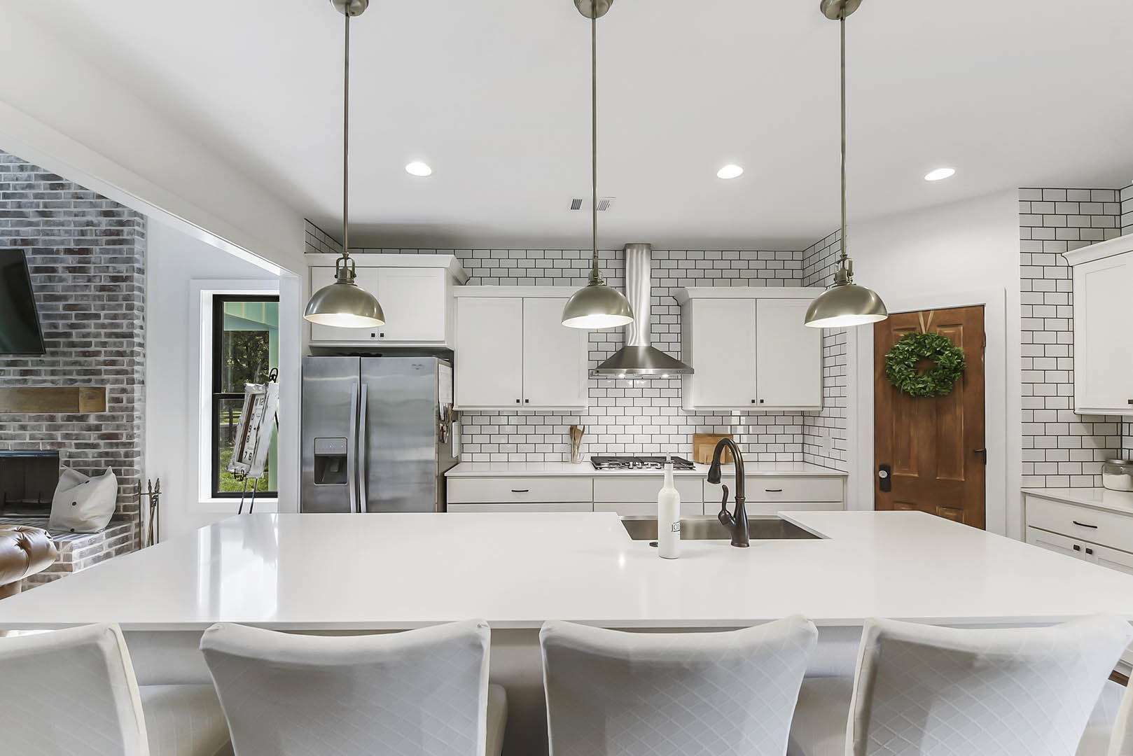 Spacious kitchen featuring a large central island with white quartz countertop, stainless steel refrigerator, modern cabinetry, built-in sink, and pendant lighting overhead