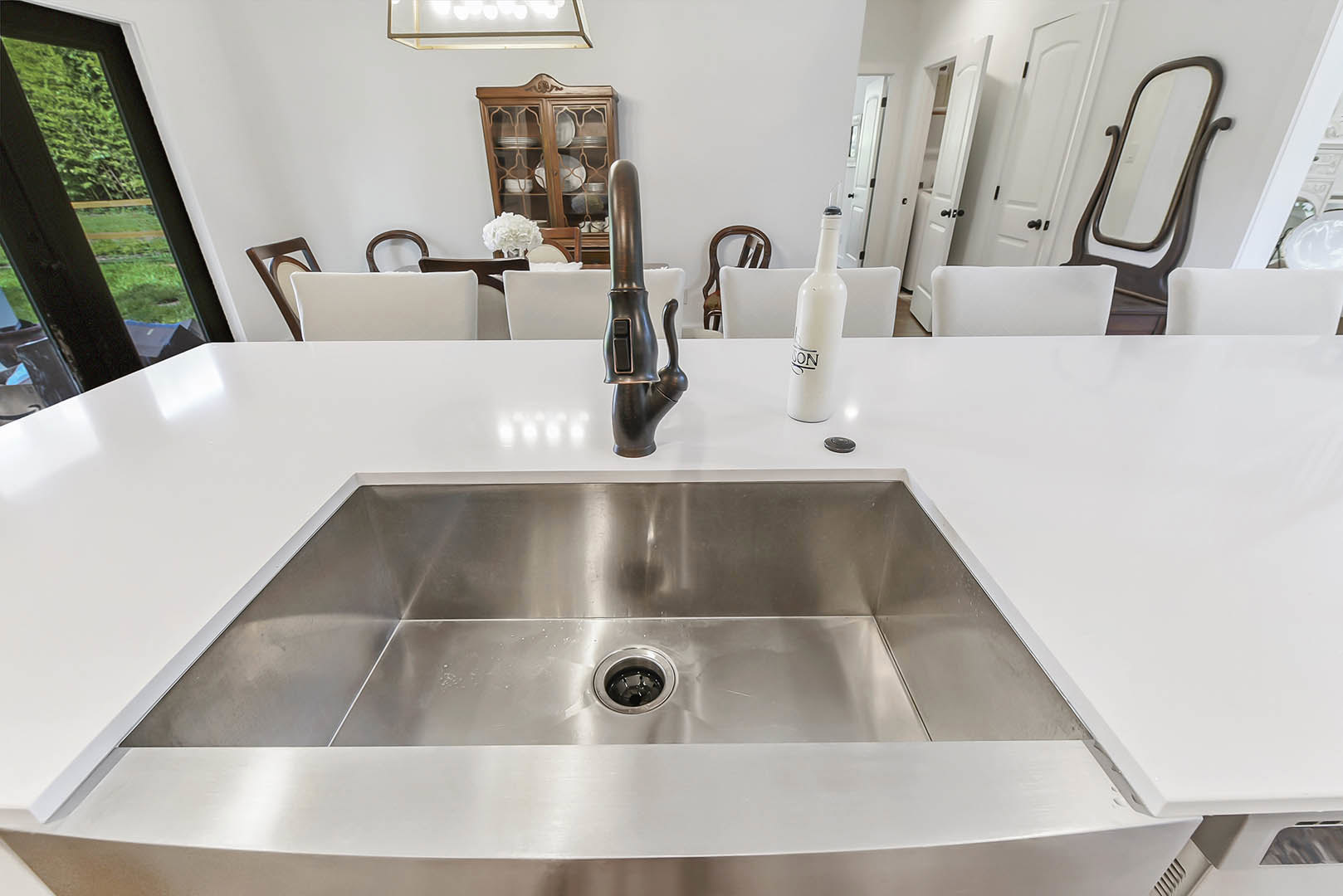 White bathroom countertop with undermount sink, chrome faucet, and a white bottle with black lid against a light wall