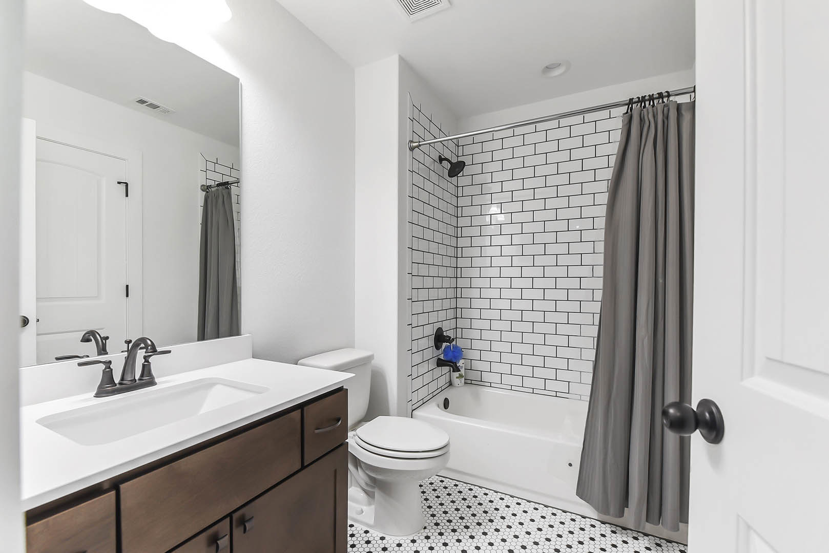 Bathroom with white subway tile walls, grey shower curtain, white bathtub, modern toilet, white sink with chrome faucet, and light wood vanity cabinet