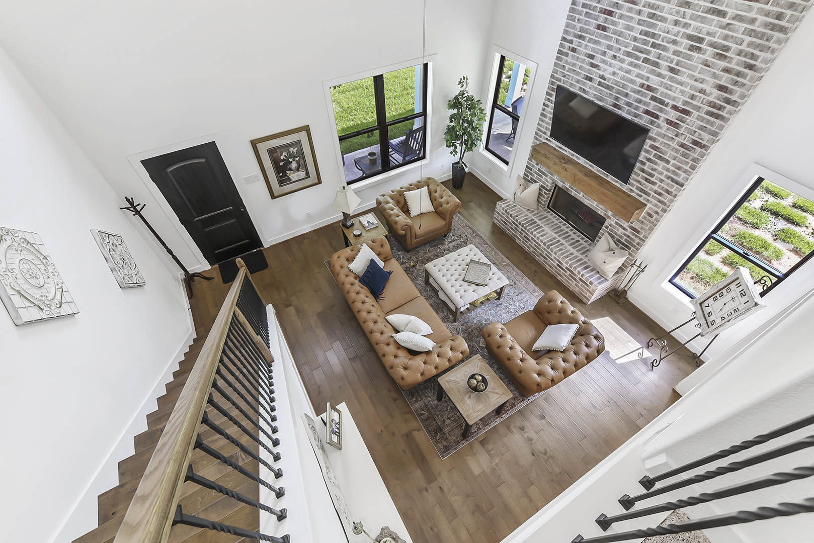 Living room with a brick fireplace, mounted TV, gray couch with patterned pillows, brown leather chair with a white pillow, hardwood floors, and a close-up of a book on a side