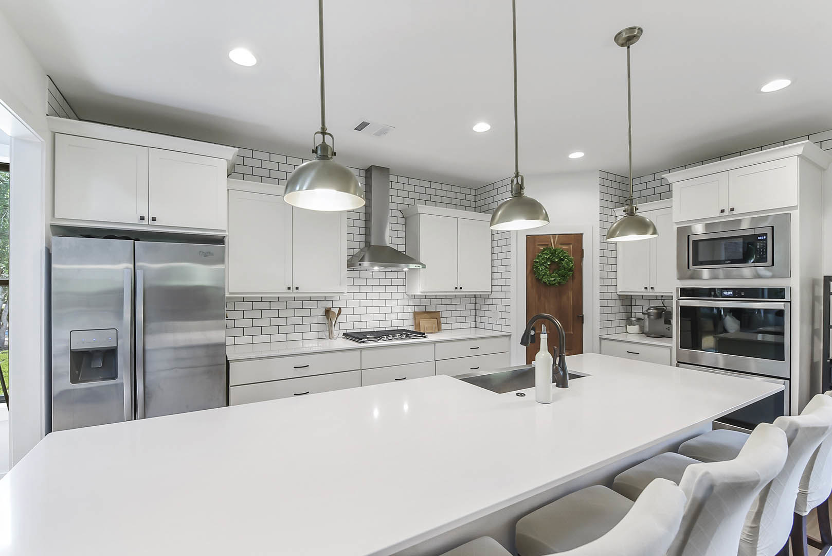 Spacious kitchen featuring a large white island with built-in sink, stainless steel refrigerator, white cabinetry, and light countertops