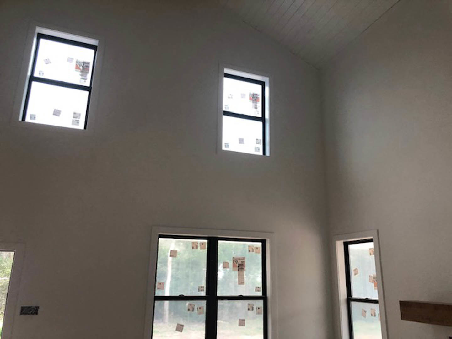 Room with large wood ceiling, multiple windows featuring sticker labels, white plaster walls, and daylight filtering through glass.