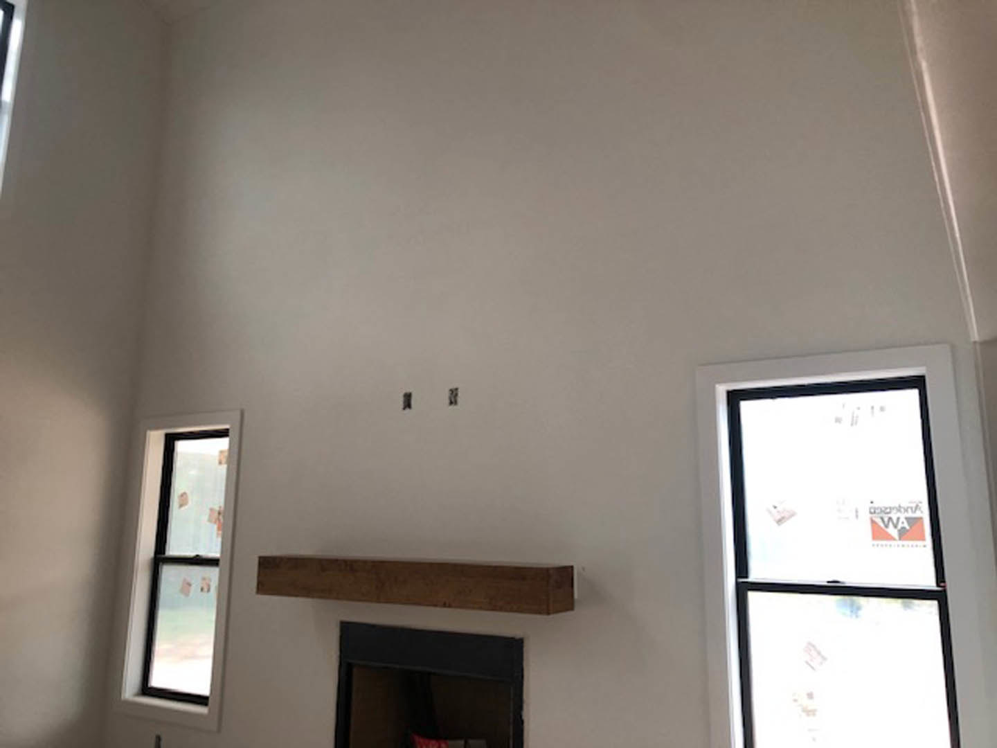 Plaster fireplace with built-in shelf in a den, black table topped with a red decorative object, white walls, ceiling, and windows with papers and stickers attached