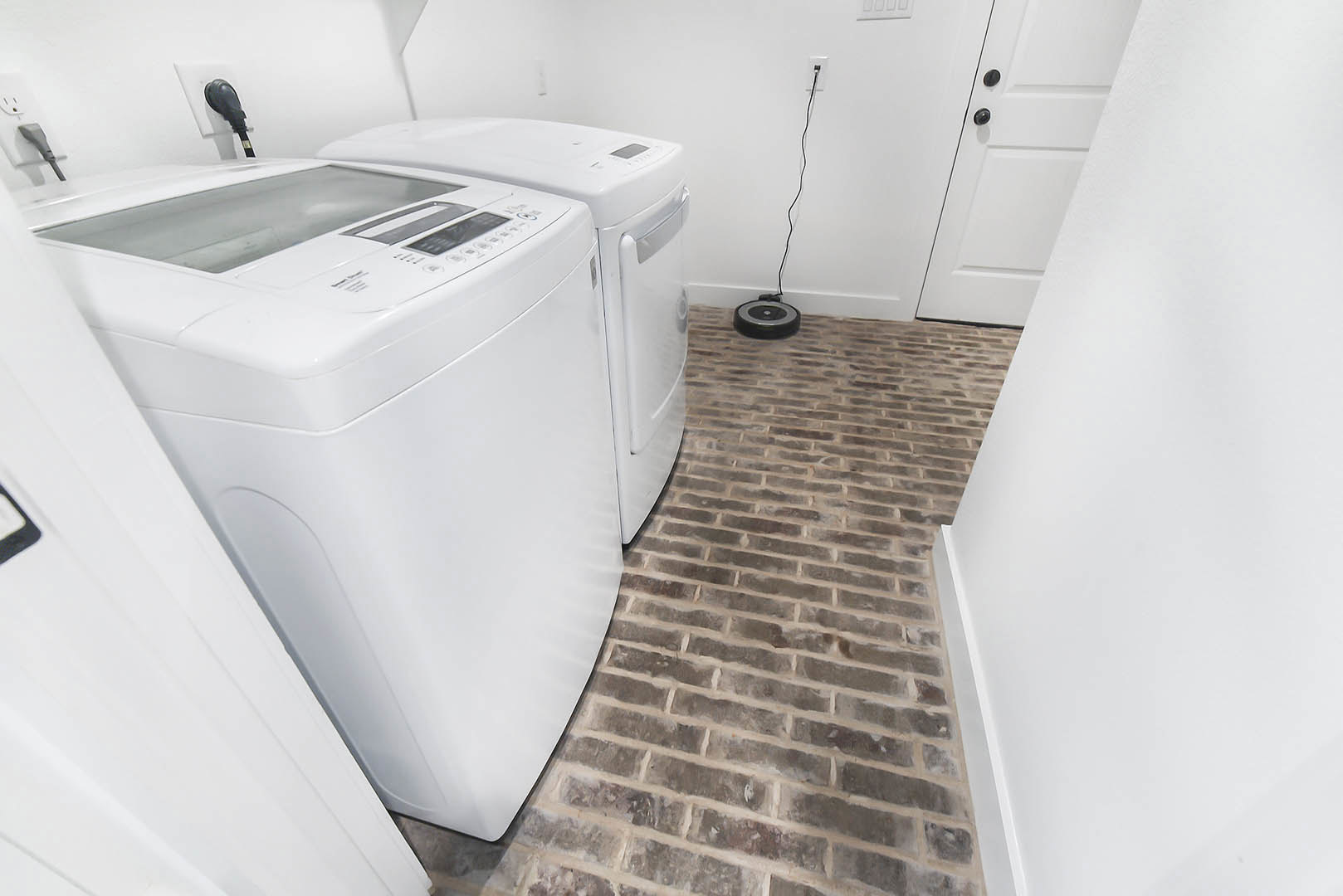 Front-loading white washing machine and dryer set side by side in a laundry room with light-colored walls and tile flooring.