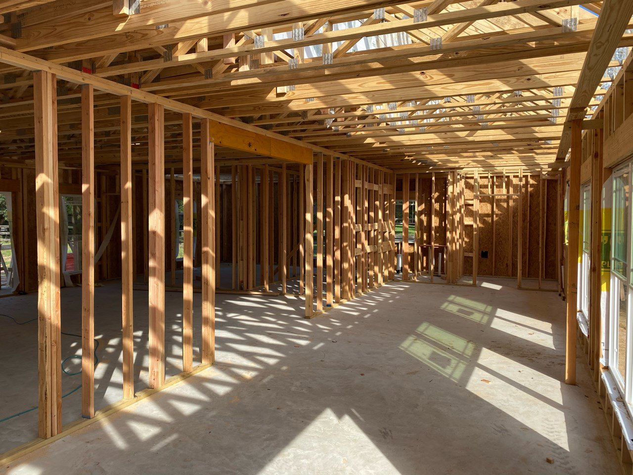 Wood-framed house under construction with exposed beams and unfinished concrete floor
