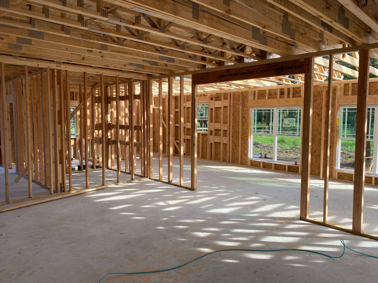 Exposed wood ceiling beams, unfinished concrete floor with blue hose, large window overlooking grass and dirt