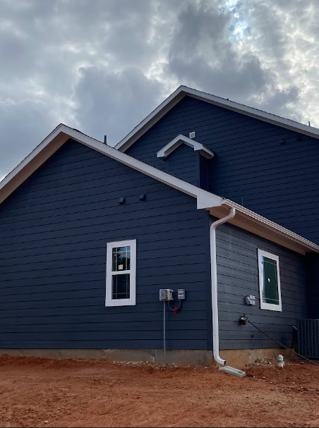 Two-story house with blue horizontal siding, white trim, gabled roof, multiple windows, and landscaped front yard under partly cloudy sky