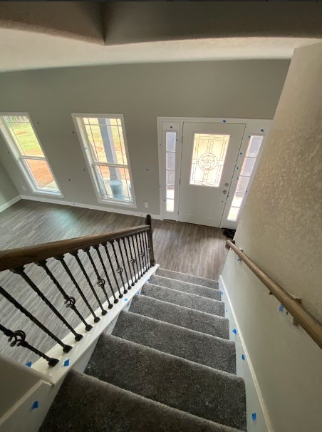 Wood staircase with white balusters and handrail, large window providing natural daylight, neutral walls, and ceiling fixtures in a modern residential interior.