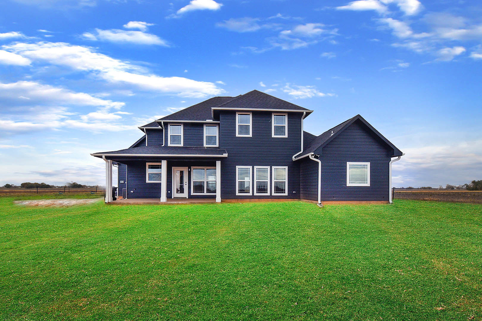 Blue house with white trim and window frames, manicured green lawn, partly cloudy sky in background