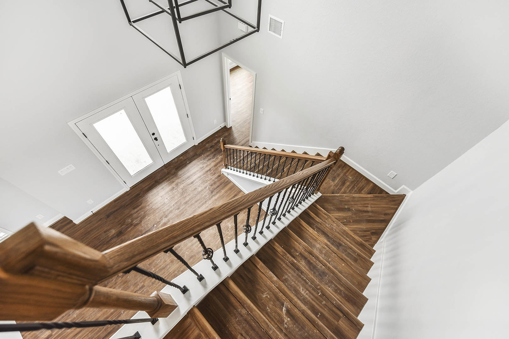 Staircase with wood flooring, wood railings, and white plaster walls, white double doors with glass panels, metal handrail, and white wall vent