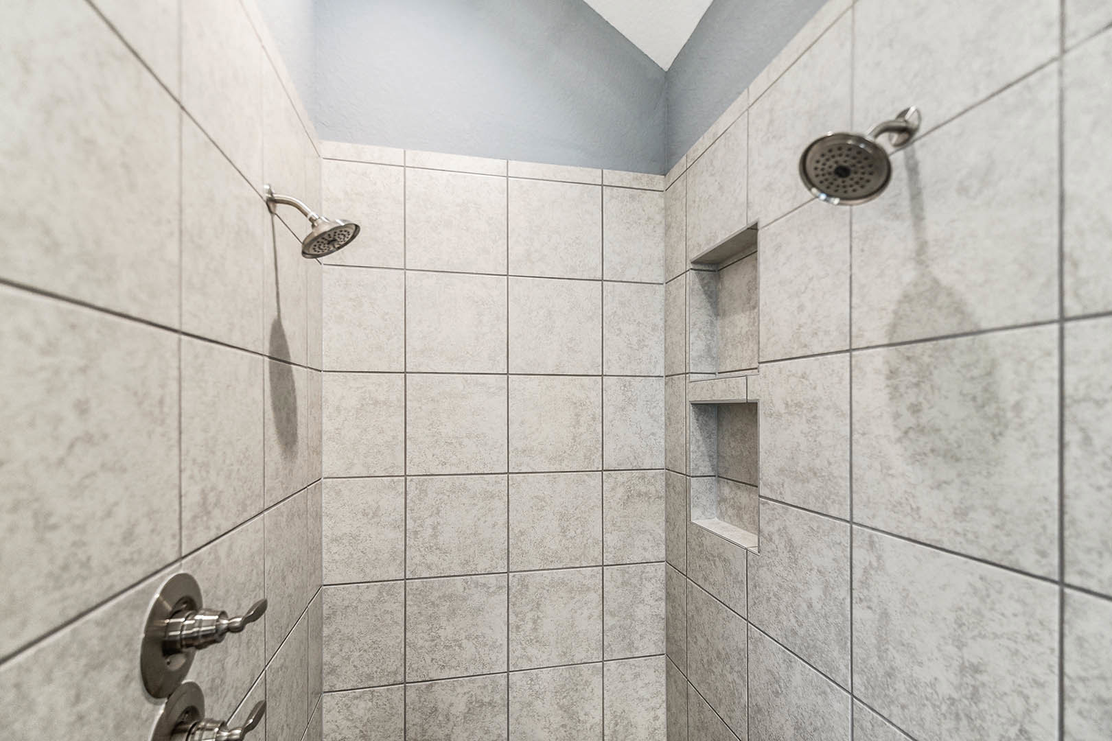 Modern bathroom shower with chrome shower head mounted on white tile wall, partial view of glass door and ceiling