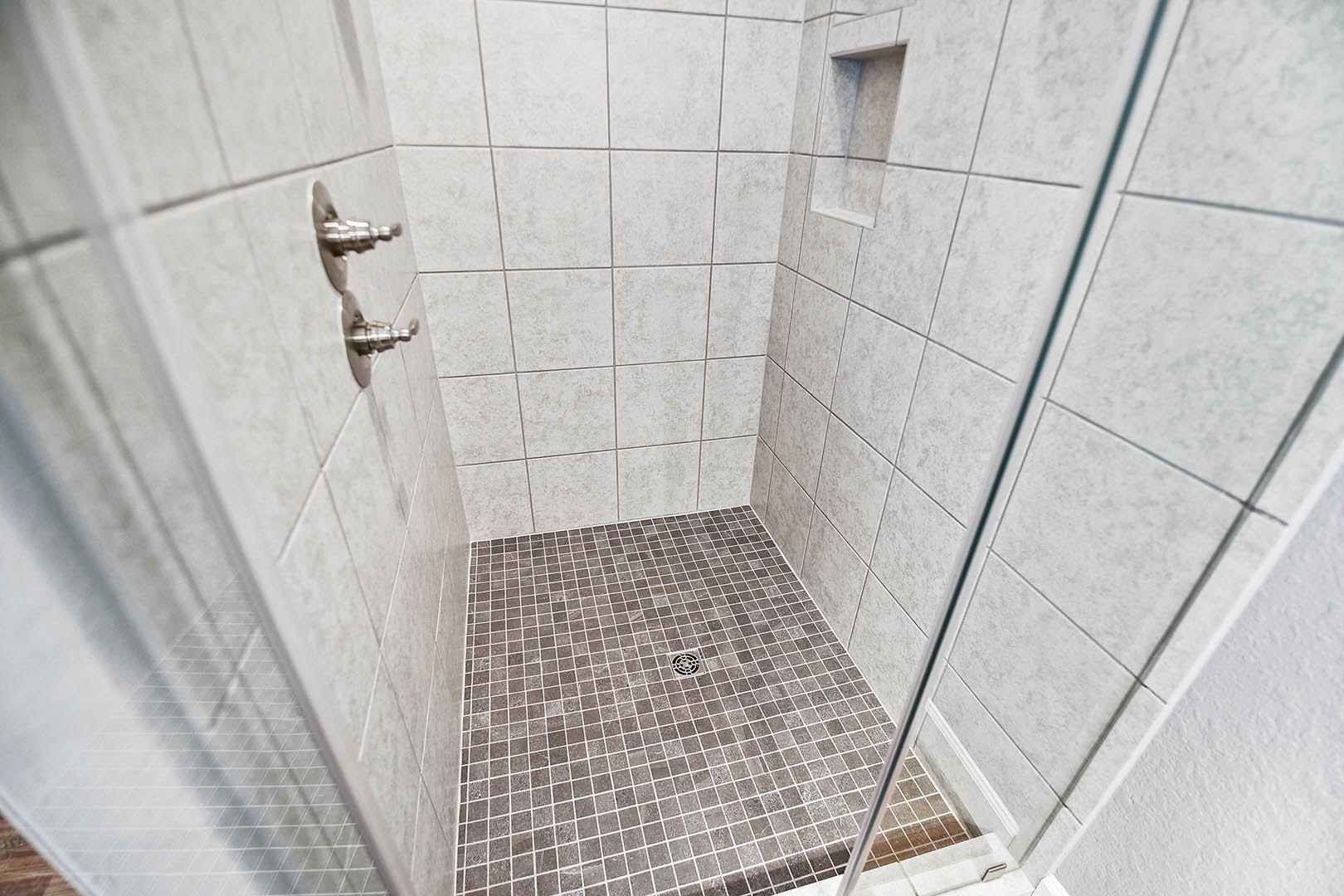 Walk-in shower with glass door, chrome shower head, large-format gray tile walls, and tiled floor with central drain