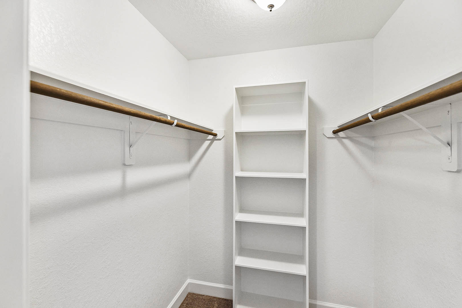 White built-in shelves against a plaster wall, wooden bar accent on door, carpeted floor, and white ceiling in a modern interior room.