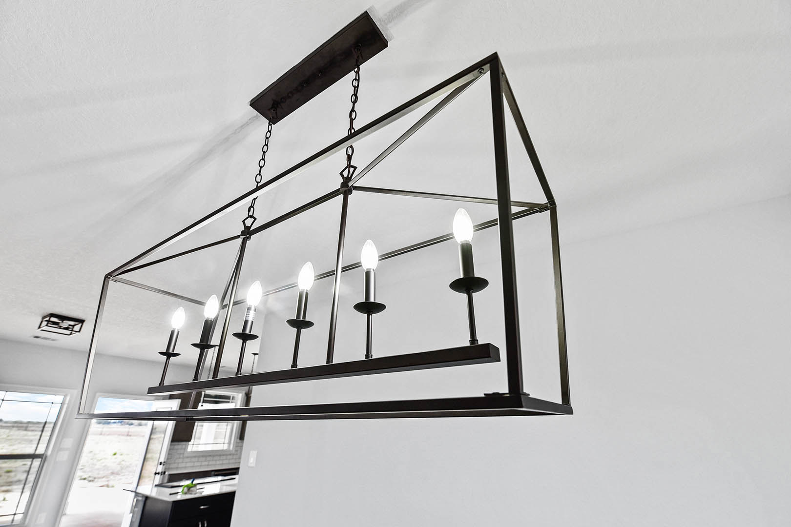 Iron chandelier with candle-style lights hanging from a black ceiling, outdoor setting visible in background