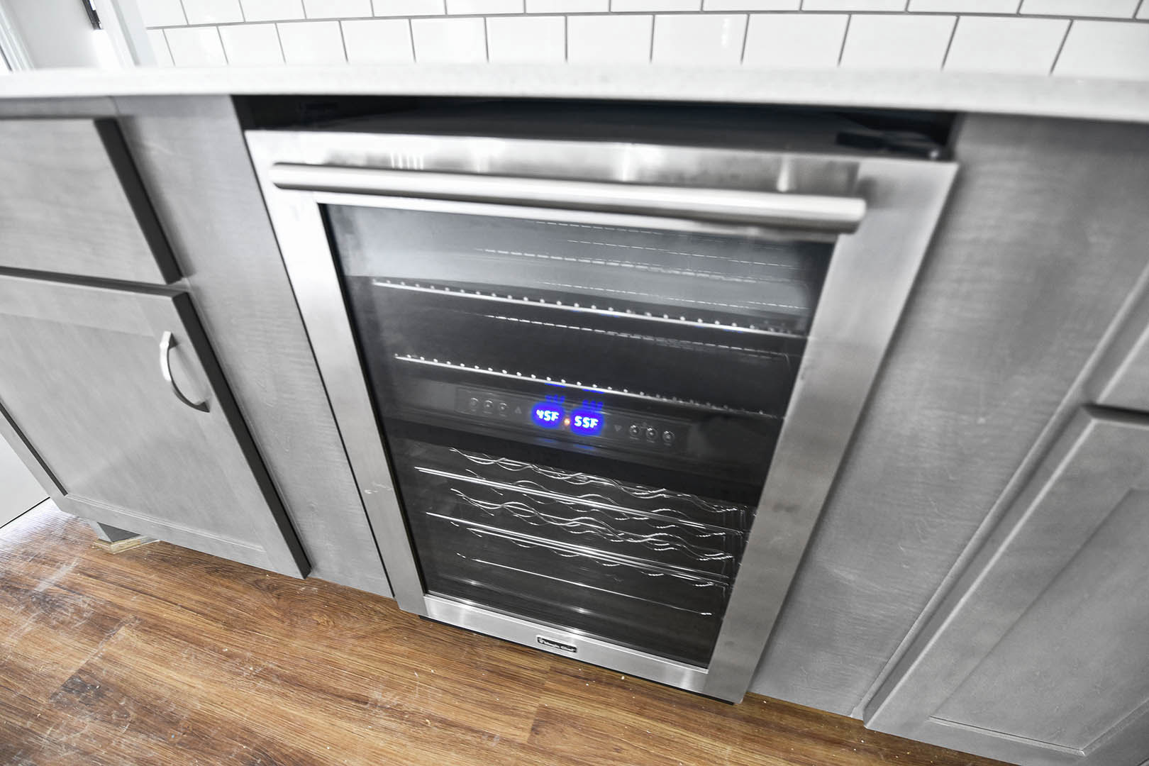 Stainless steel oven with glass doors set into white cabinetry, adjacent to a wine rack and kitchen appliances