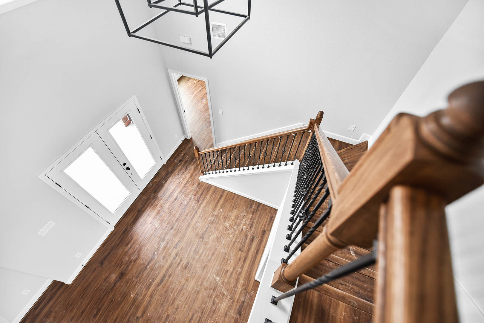 Wood staircase with white risers and handrail, hardwood flooring, white double doors, metal shelf with light switch, white wall vent, plaster walls