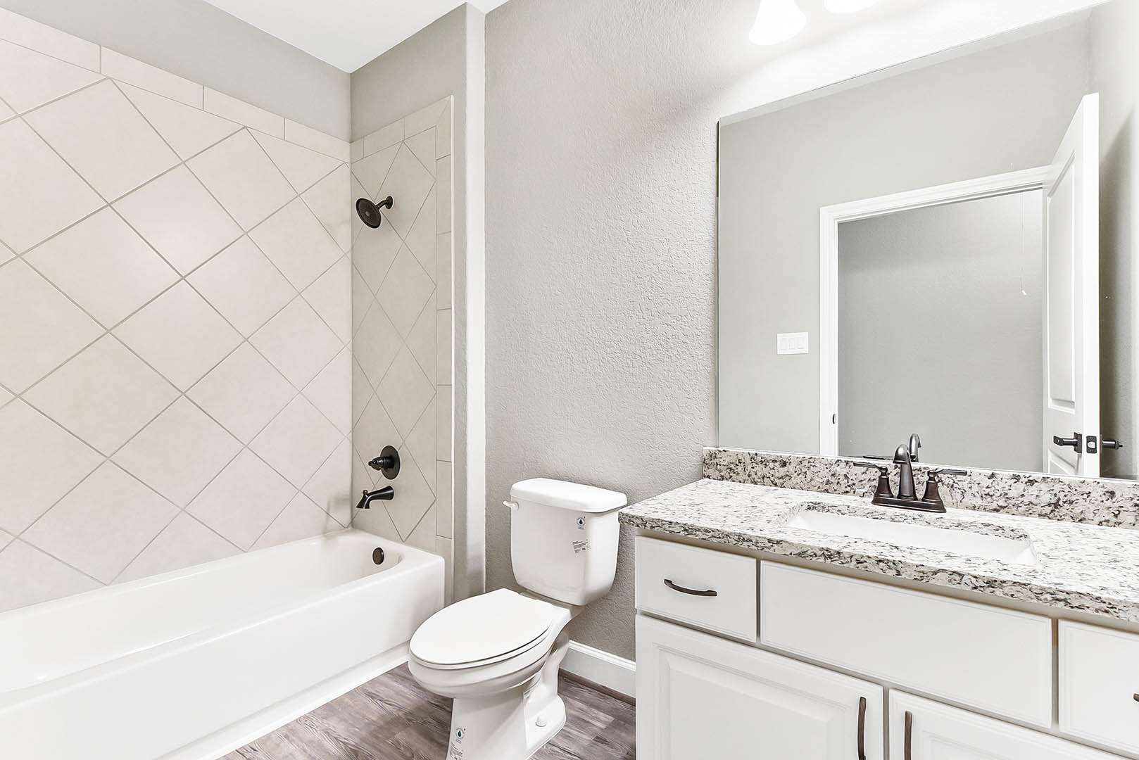 Bathroom with white toilet, rectangular sink on stone countertop, wall-mounted faucet, large mirror, tiled shower with glass door, and built-in bathtub.