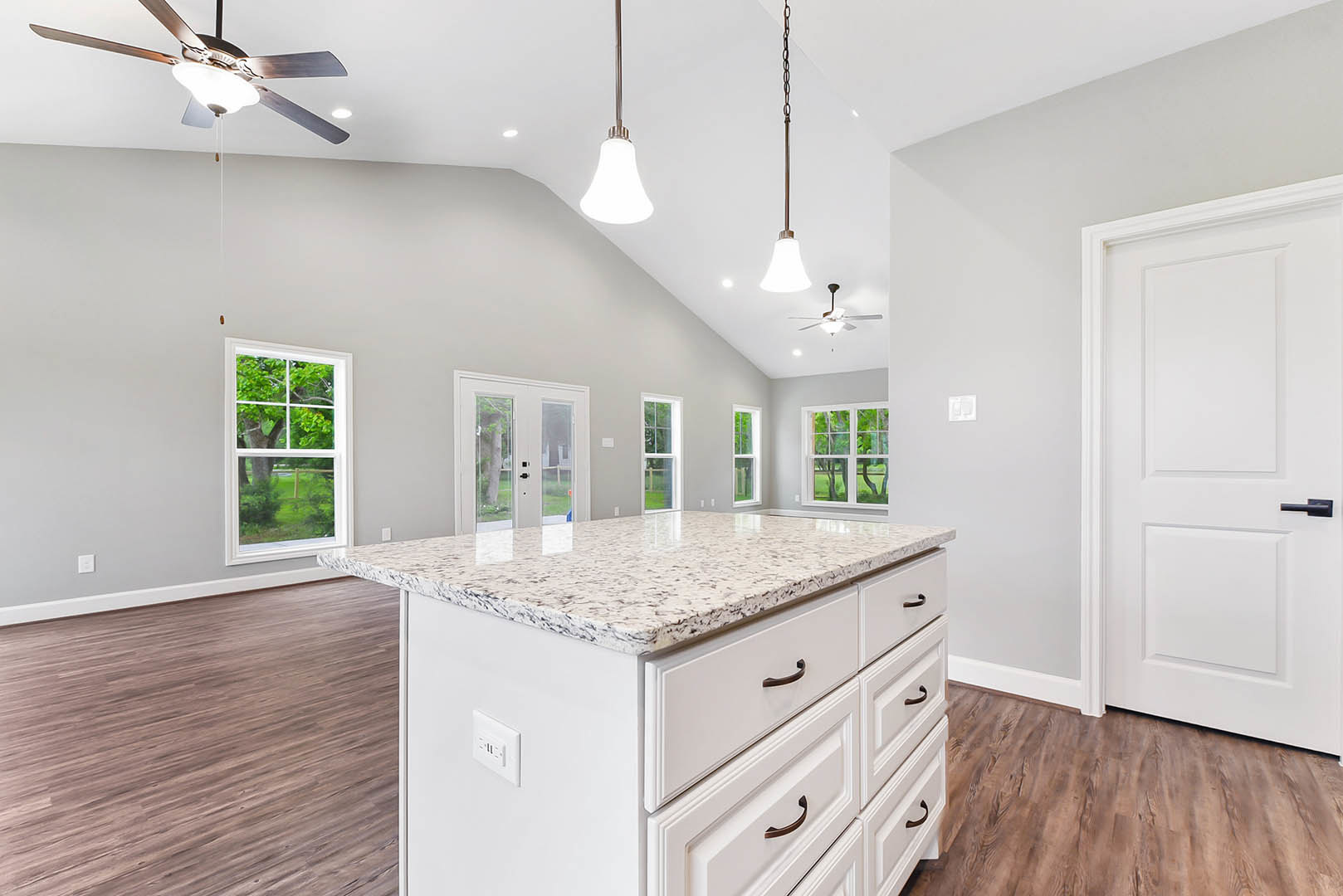 Marble kitchen island with built-in sink and drawers, ceiling fan with light above, white cabinetry, window overlooking tree and lawn, white door with black handle, pendant light