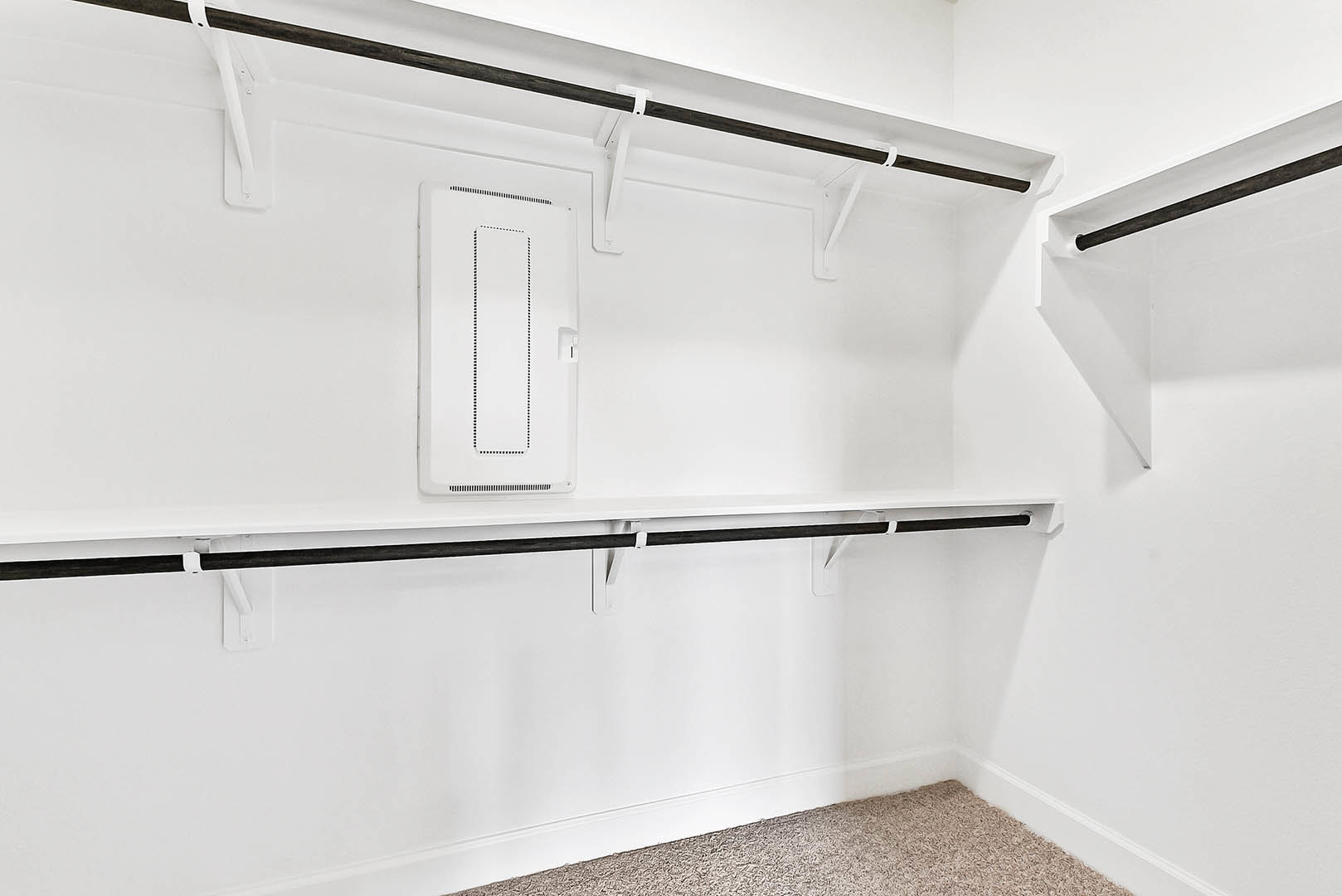 White closet with black shelves, white door with black hardware, light carpet flooring, white pipe along wall, minimal black and white accents