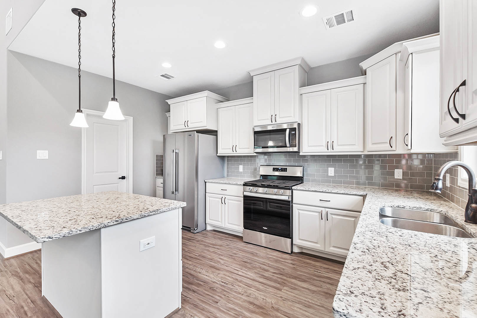 White kitchen cabinets, granite countertops, stainless steel refrigerator, black stove, open microwave door, close-up of sink