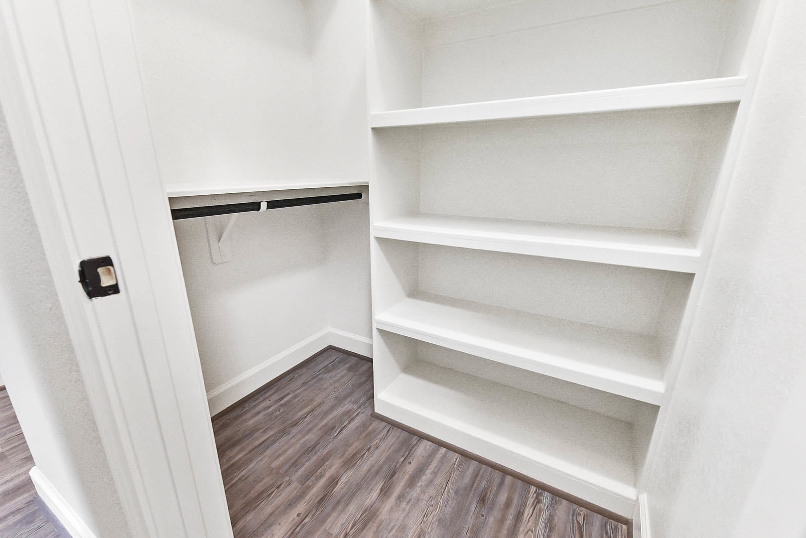 Walk-in closet with white built-in shelves, light wood plank flooring, and smooth white walls
