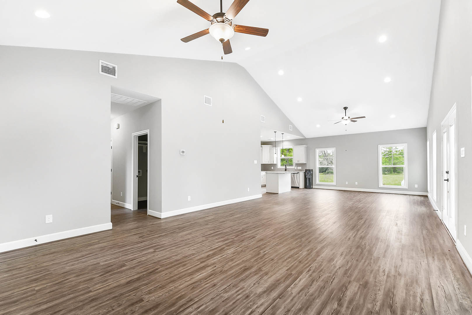 Spacious room featuring wood flooring, white walls, ceiling fan with light fixture, large window overlooking green field and tree, white door with black handle