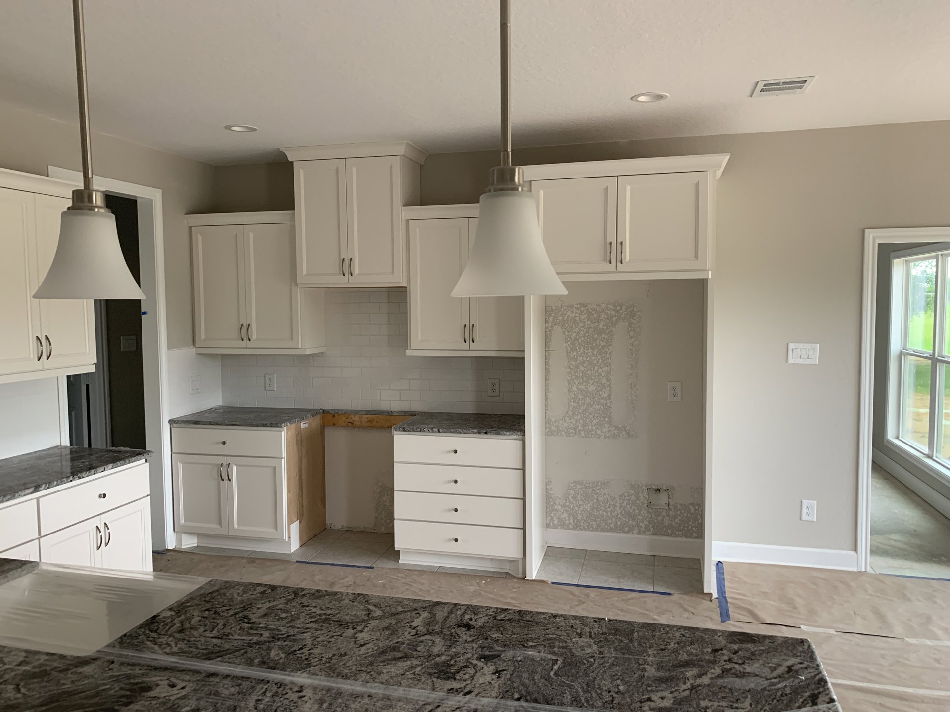 Kitchen with white shaker cabinets, marble countertops, stainless steel sink, and modern light fixture; window overlooks green lawn.