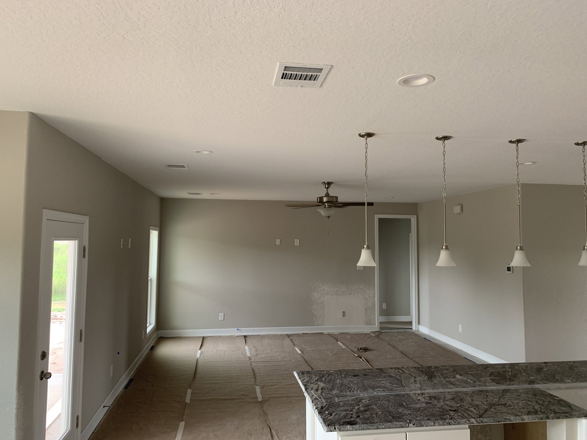 Open kitchen with light tile countertop, stainless steel sink, plaster walls, ceiling fan with chain, and window overlooking grassy field.