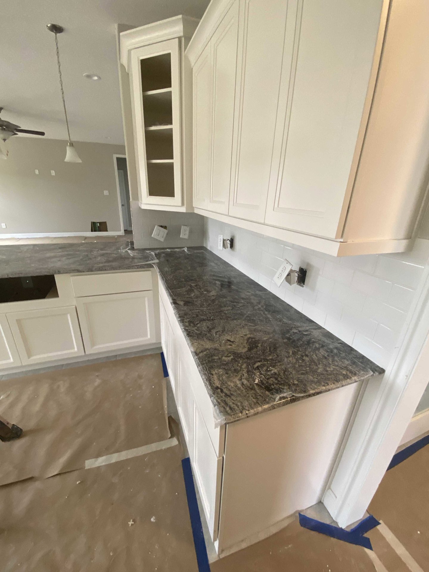 White kitchen cabinets with marble countertops, white tile backsplash, built-in shelving door, black countertop section, ceiling fan with light fixture, stainless steel appliances