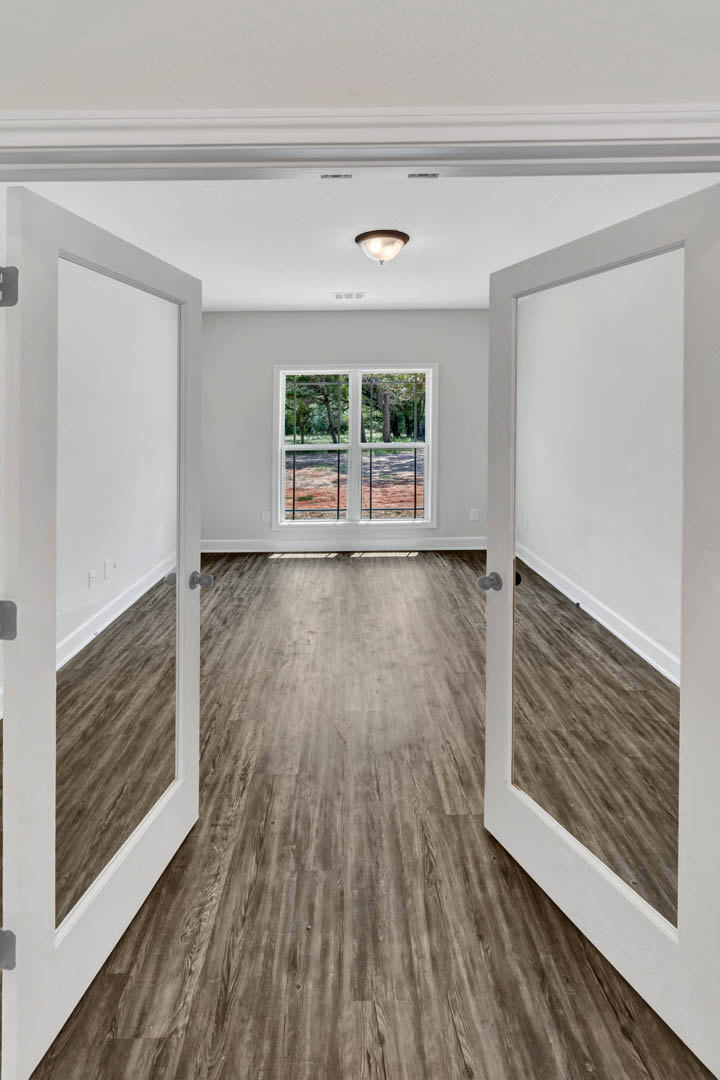 White walls and wood flooring in a room featuring two white doors and a window with a view of green trees.