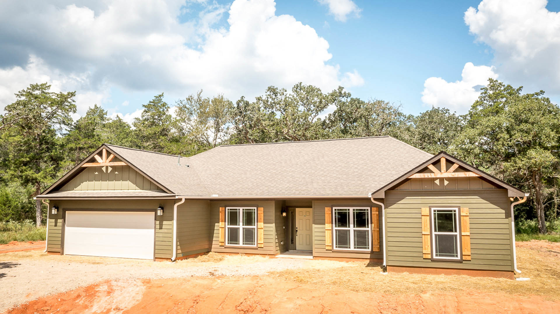 Two-story home with attached garage, paved driveway, white front door, large windows, white siding, and mature trees in the yard