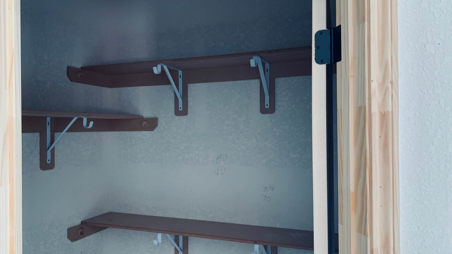 White metal shelf bracket mounted on a closet wall with a hook and handle, surrounded by white walls.
