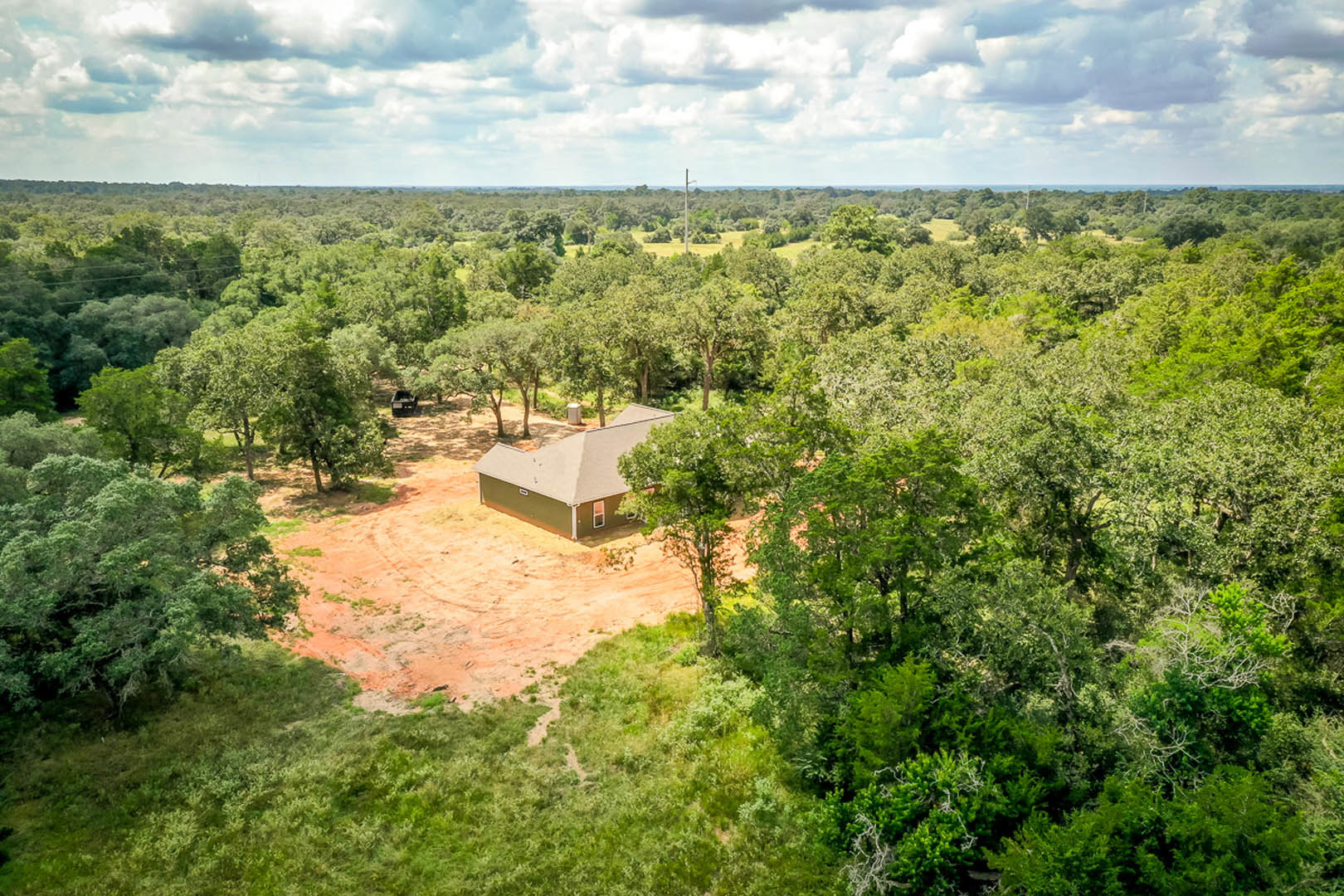 Modern custom home surrounded by tall trees, grassy lawn, and dense forest under a cloudy sky